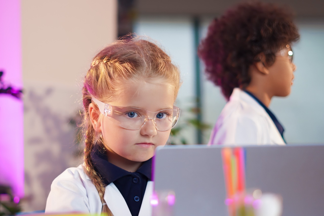 girl elementary student in lab coat in front of computer